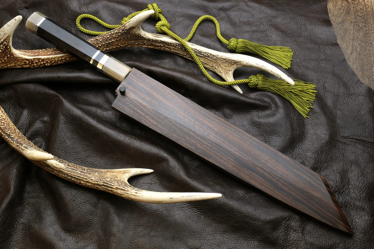 Kiritsuke knife with dark handle, horn sheath, and green cord tassel.