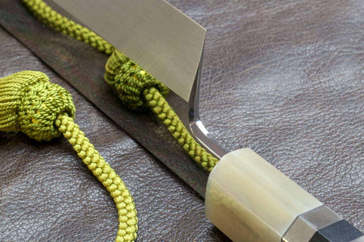 Knife handle close-up with ivory wrap and silver-toned bands, green cord.