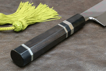 Japanese-style kitchen knife with dark handle and wavy steel blade, green tassel cord