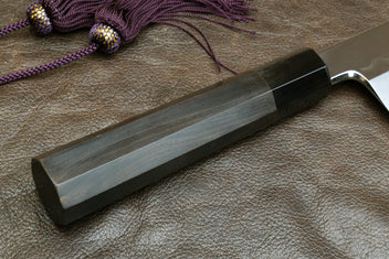 Kiritsuke knife with dark handle and mirror-polished steel blade, side view