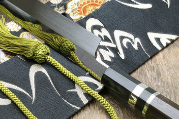 Japanese kitchen knife with mirror-finished blade, dark handle, and green cord tassel