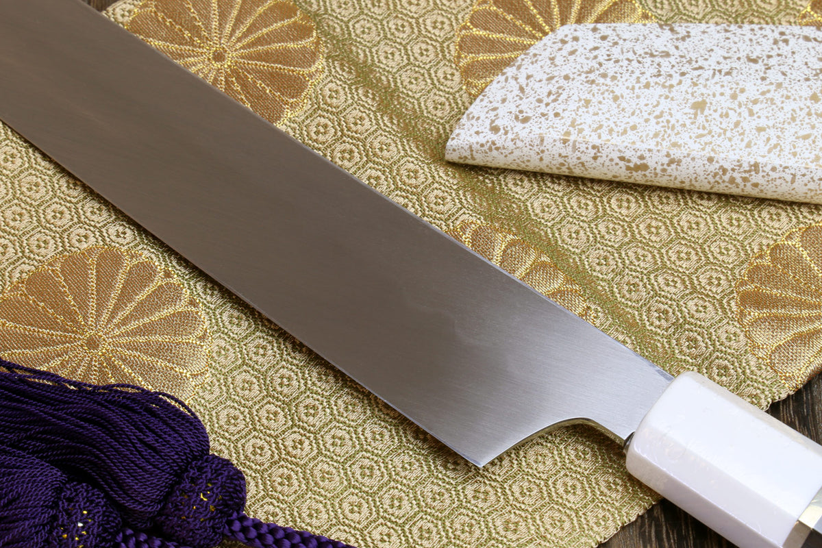 Japanese sushi sashimi knife with silver blade and white handle, on patterned cloth