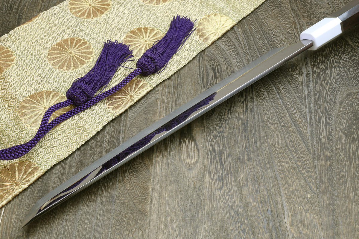 Japanese sushi sashimi knife with silver blade, dark handle, and purple tassel on cloth