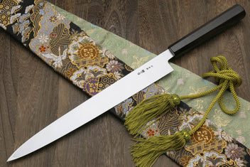 Japanese kitchen knife with mirror blade and black handle, ornate pouch and green tassel ties