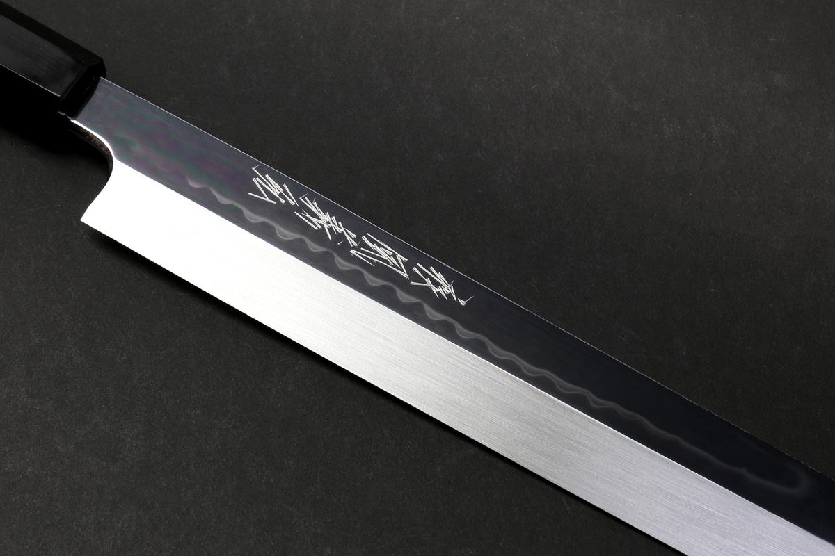 Japanese knife blade close-up with mirror-finished steel and etched pattern near the spine.