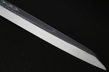 Japanese knife blade close-up with mirror finish and faint etched pattern along the back edge.