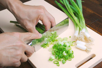 Nakiri knife chopping scallions on a cutting board, hammered Damascus blade.