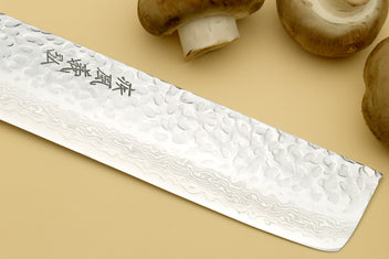 Nakiri knife blade close-up, hammered Damascus steel with engraved mark.